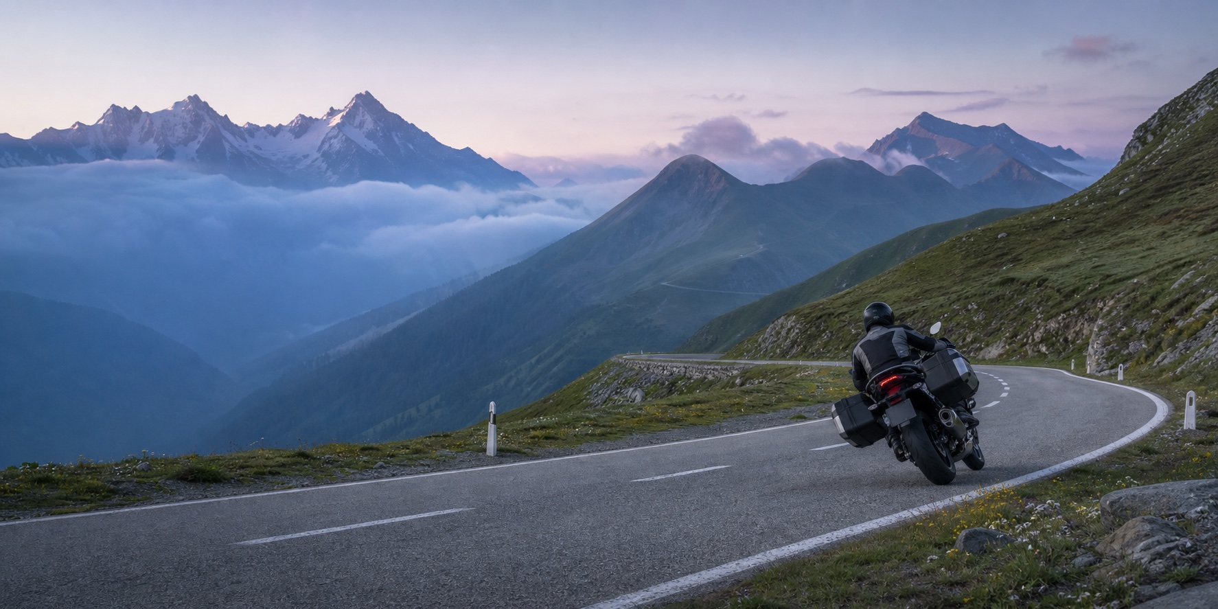 A touring motorcyclist follows a sweeping road through a quiet Alpine pass.